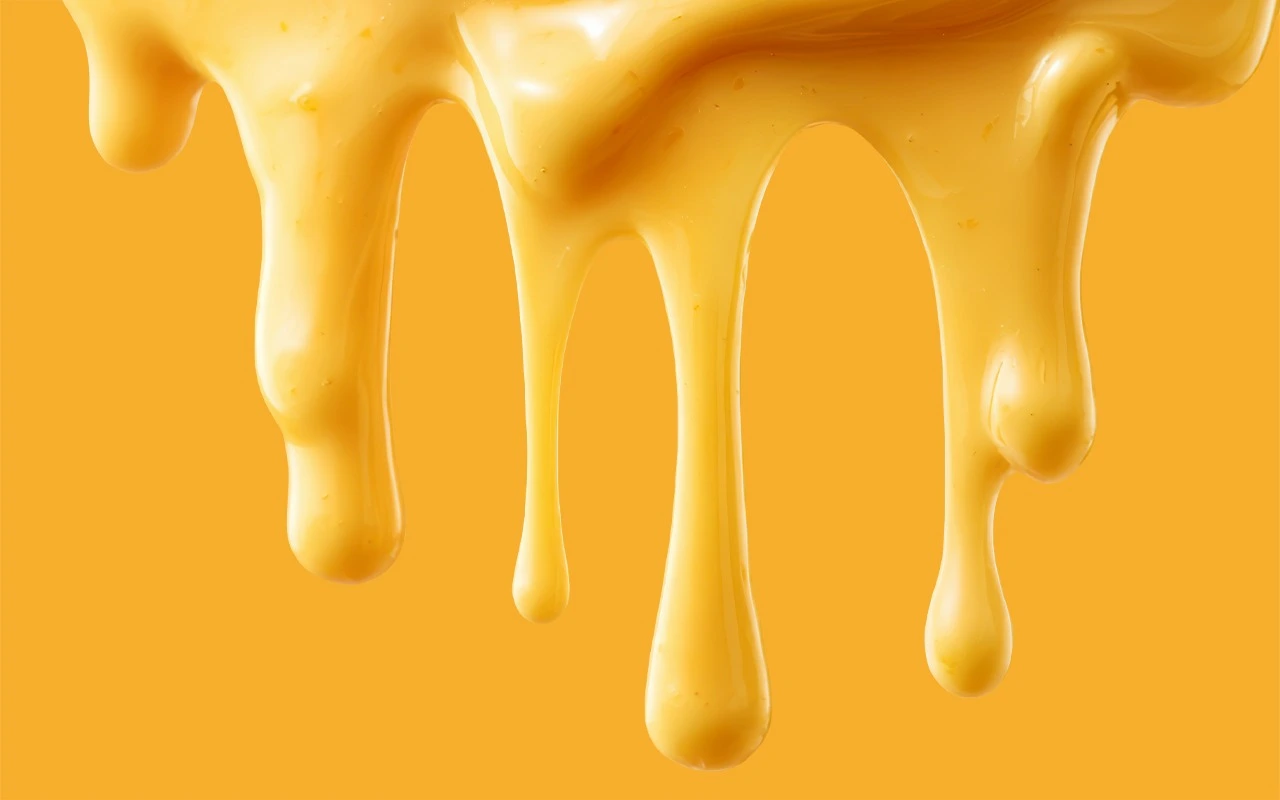 Glossy golden honey dripping in long streams against a warm yellow background